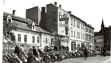 Účastníci motoristické soutěže "Cíl neznámý" z roku 1930 před objektem domu U Ferusů na Senovážném nám. 6. v Českých Budějovicích. Foto: Archiv SOA Třeboň. 