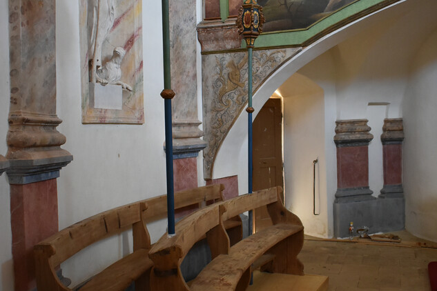 Pohled na lavice s lucernami a postavníky, v pozadí kruchta s obrazy sv. Isidora