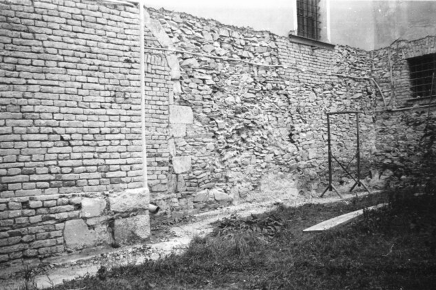 Loštice, kostel sv. Prokopa. Celkový pohled na JV zeď presbytáře z roku 1993. Vlevo patrná dochovaná část románského bočního vstupního portálu, uprostřed mladší vyzdívka statické poruchy.